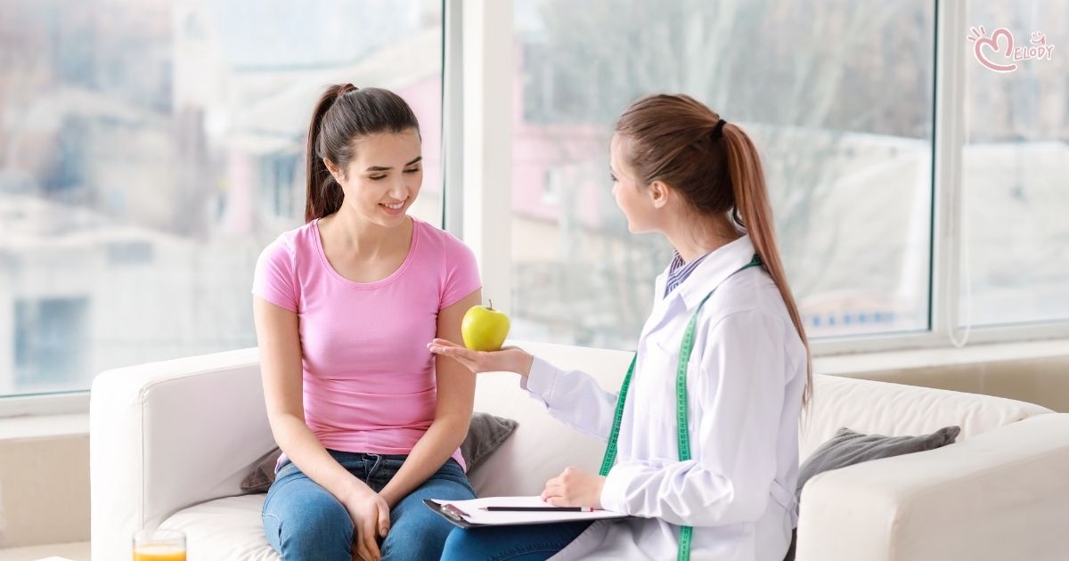 A female doctor talks with a young woman seated on a sofa.